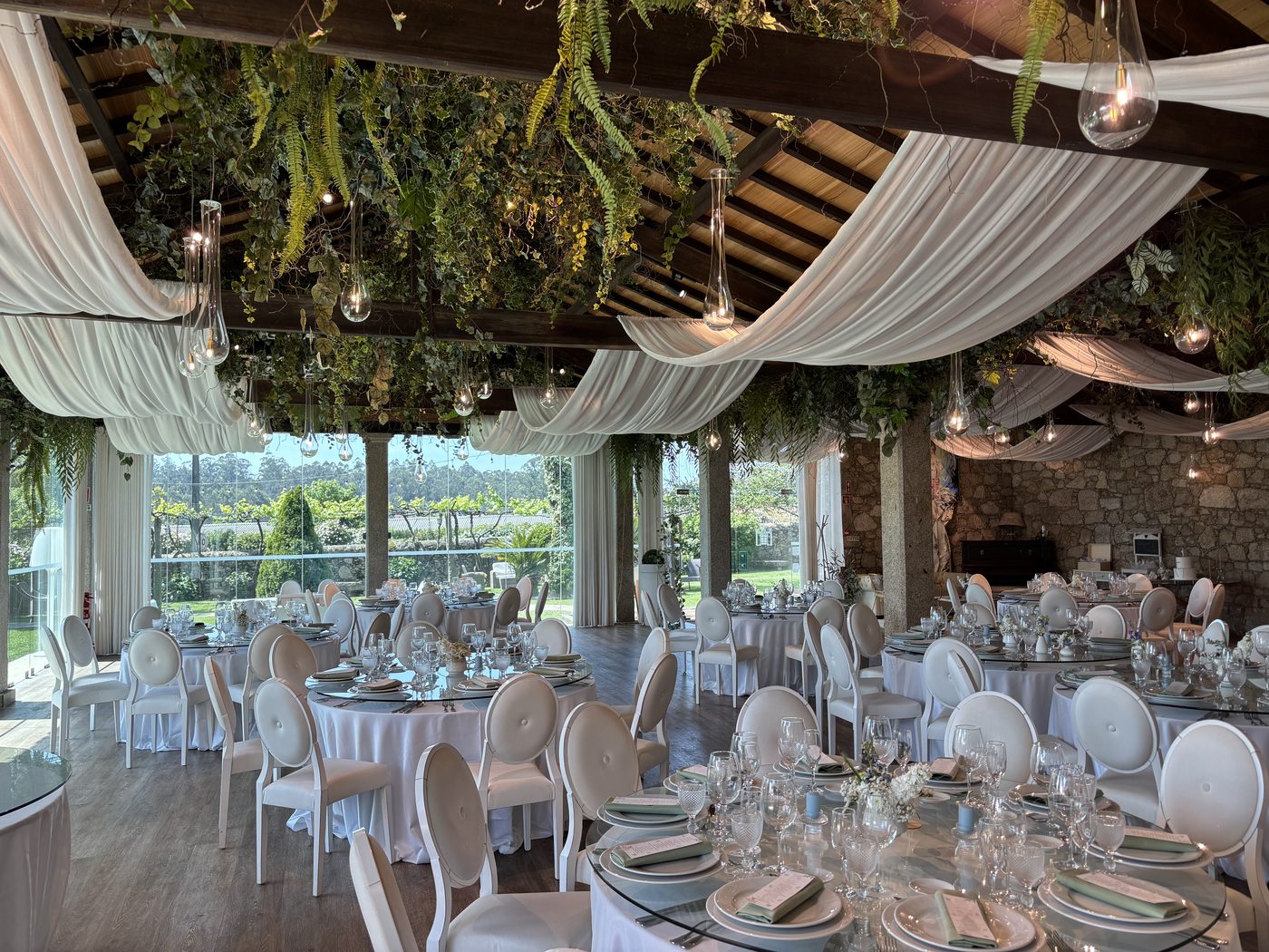 Salão rústico em pedra da Quinta São Miguel de Arcos, decorado para casamento, com mesas postas, drapeados e vegetação suspensa.